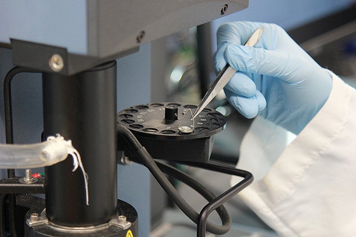 A close up of a hand in a blue latex glove holding tweezers on a machine