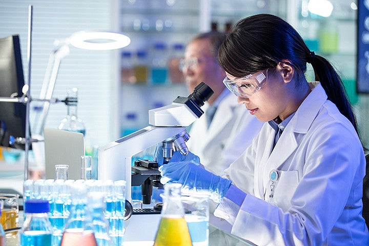 Multiple people wearing white lab coats working on scientific equipment in a lab