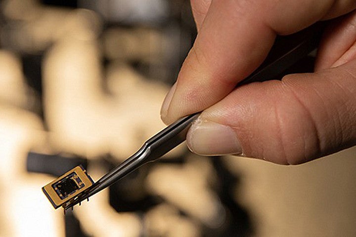 A hand holding a tiny device with tweezers