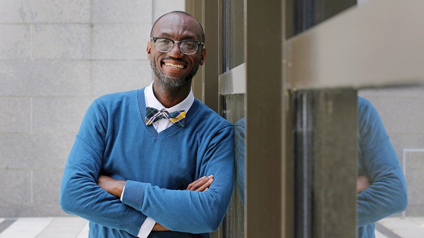 Dr. André Isaacs smiles and leans against a wall