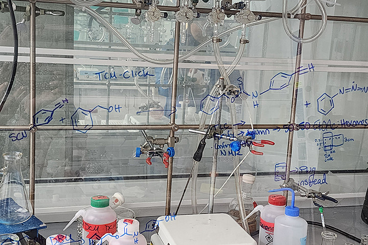 A scientific equation written on a clear glass window in front of scientific equipment